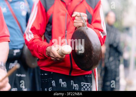 Bajawa, Nusa Tenggara Timur, Indonesia - 09 July 2026: View of a musician playing a traditional gong while wearing a red jacket and patterned sarong. Stock Photo