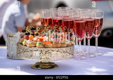 Elegant outdoor catering setup on a white tablecloth, featuring pre-poured drinks and bite-sized appetizers ready for a celebration Stock Photo