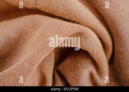 Horizontal close up of a soft brown cotton twill fabric showing detailed diagonal weave patterns on a folded textile surface with warm shadows. Stock Photo