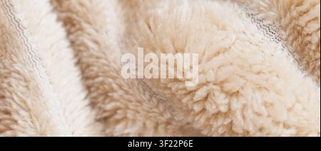 Panoramic close up of a fluffy beige sherpa fleece fabric showing soft delicate curly wool fibers on a warm cozy blanket surface with copy space. Stock Photo