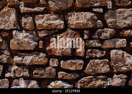 Horizontal close up of an old rustic stone wall texture with brown weathered rocks and dark cement joints on a sunny day showcasing architectural deta Stock Photo