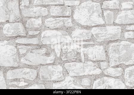 Horizontal close up of a bright white washed stone wall texture featuring rough limestone blocks and grey mortar joints on a clean rustic building ext Stock Photo