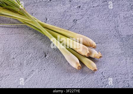 Fresh lemongrass stalks arranged diagonally on textured gray concrete background. Natural lighting highlights pale green cream tones. Minimalist food Stock Photo