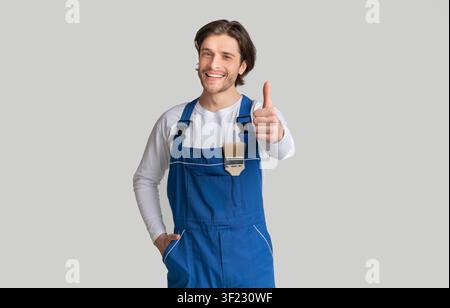 Painting Works. Young Handyman With Paintbrush In Pocket Showing Thumb Up Stock Photo