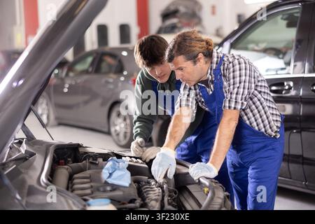 Two mechanics examining car engine under open hood in workshop Stock Photo