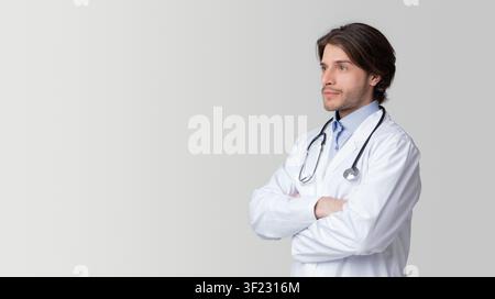 Portrait Of Thoughtful Male Doctor Standing With Folded Arms And Looking Away Stock Photo