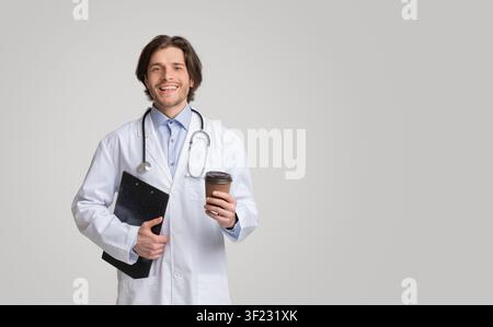 Portrait of young smiling doctor holding medical chart and takeout coffee Stock Photo