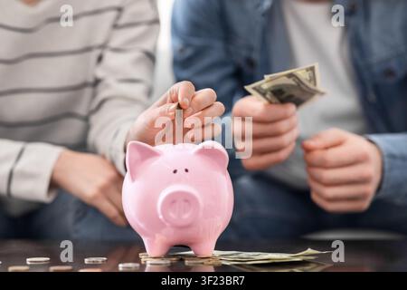 Young family saving money to piggybank at home, close up Stock Photo