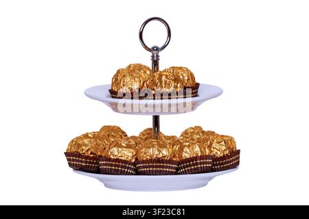 Pastries, desserts and sweets. Chocolate candies wrapped in golden foil on a two-storey etagere isolated on a white background. Clipping path. Decorat Stock Photo