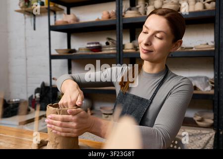 Beautiful woman focuses on her craft while molding clay in her cozy studio Stock Photo