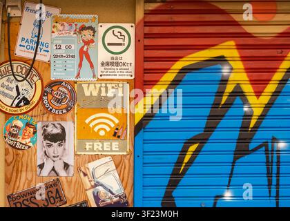 Close-up street view of a blue corrugated metal roller shutter door covered in graffiti and sticker labels, Osaka, Japan. Stock Photo