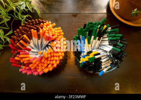 Markers of different colors are neatly arranged in two bowls on a wooden table. One bowl has warm colors while the other has cool colors. Some green p Stock Photo