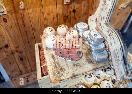 A wooden display holds various handmade soaps and candles. The soaps are stacked neatly while the candles are placed in tins. This setup is inside a c Stock Photo