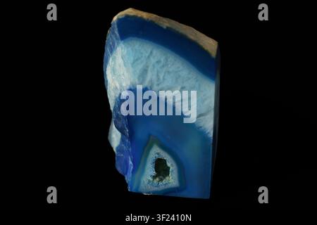 Blue and white banded agate slice with natural crystal inclusions. Smooth polished surface against black background. Stone features concentric rings a Stock Photo