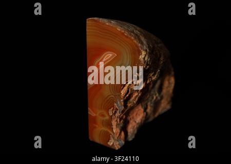 Polished slice of agate stone with rich orange and brown banding. Stone shows natural concentric patterns and rough edges. Stock Photo
