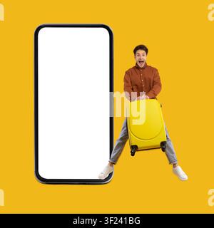 Excited Young Man With Yellow Suitcase Sitting On Smartphone Mockup, Traveling Concept Stock Photo
