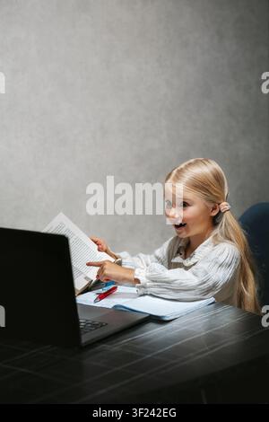 Elementary school child student studying online on laptop, curious girl reading and writing during interesting online lesson homeschooling digital lea Stock Photo
