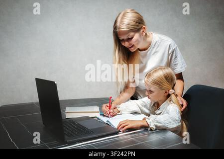 Mother helping her child girl writing and study in online school using laptop at home, homeschooling and digital education kid learning with modern te Stock Photo