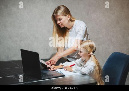 Mother helping her daughter study lesson in online school with laptop at home, child using homeschooling digital education family lifestyle learning t Stock Photo
