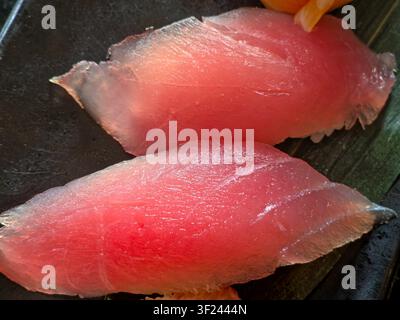 High-angle close-up of two Akami nigiri sushi pieces with glossy red-pink tuna slices on a dark textured plate, highlighting fresh seafood and Japanese Stock Photo