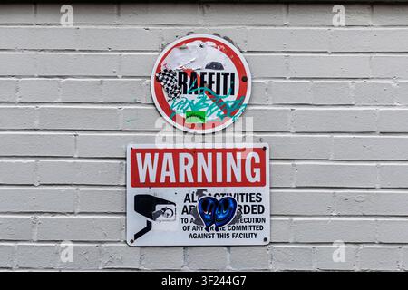 A no graffiti sign and CCTV surveillance warning mounted on a painted brick wall. Stock Photo