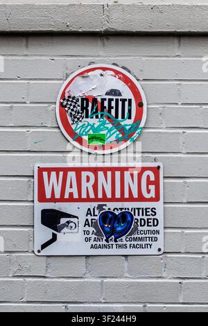 A no graffiti sign and CCTV surveillance warning mounted on a painted brick wall. Stock Photo