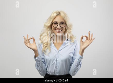 Smiling Young Blonde Woman In Glasses Showing Ok Gesture, Office Concept Stock Photo