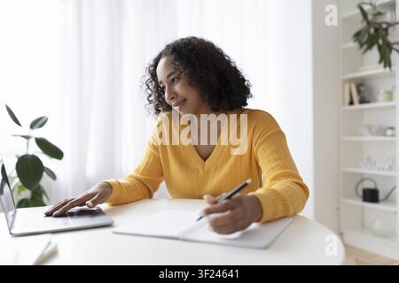 Focused Young Black Woman Working On Laptop And Taking Notes At Home, Business Concept Stock Photo