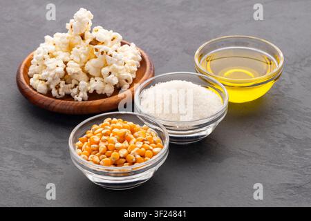 Ingredients for making sweet popcorn: corn kernels, sugar, vegetable oil, and freshly popped popcorn on a dark background with space for text. Stock Photo