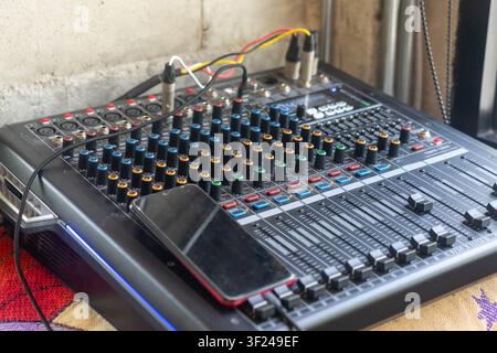 This image shows a professional audio mixing console with various controls, LED indicators, and a smartphone placed on top, used for music mixing, sou Stock Photo