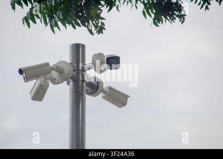 This image shows multiple security cameras mounted on a metal pole under cloudy sky, used for surveillance and monitoring outdoor areas for safety and Stock Photo