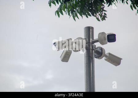 This image features a cluster of security cameras mounted on a tall metal pole, overlooking an outdoor area on a cloudy day, emphasizing security and Stock Photo