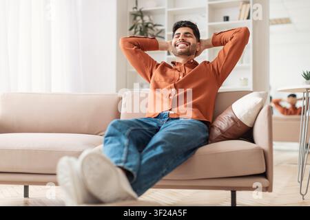 Smiling Young Hispanic Man Relaxing On Couch At Home, Positive Lifestyle Concept Stock Photo