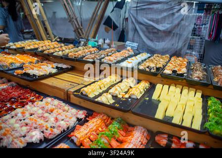 A vibrant display of assorted sushi, sashimi, and seafood delicacies arranged on wooden tables at a busy market stall, showcasing fresh ingredients an Stock Photo