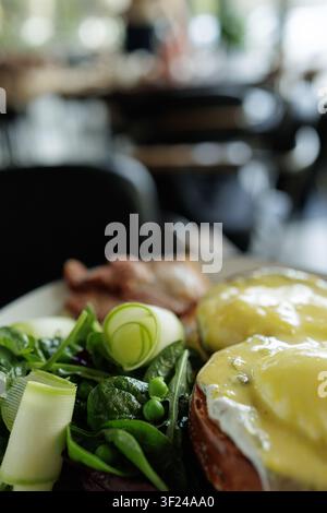 A beautifully plated dish of Eggs Benedict accompanied by a fresh salad, set in a vibrant restaurant atmosphere, perfect for food enthusiasts and culi Stock Photo