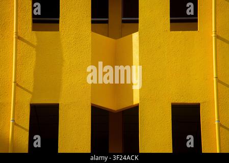 An architectural photograph showcasing a modern yellow building facade with striking geometric patterns. The image emphasizes contrast, shadow play, a Stock Photo