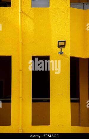 This image showcases a vibrant yellow building exterior with textured walls, multiple windows, and an outdoor security light, highlighting urban archi Stock Photo