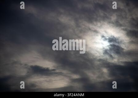 A moody, overcast sky view with dense clouds partly obscuring the sun, creating a dramatic atmosphere and highlighting the natural beauty of the sky. Stock Photo