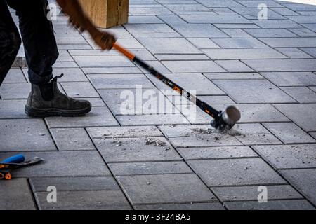 Sledgehammer striking interlocking concrete pavers during ptio removal with debris flying from the impact. Stock Photo