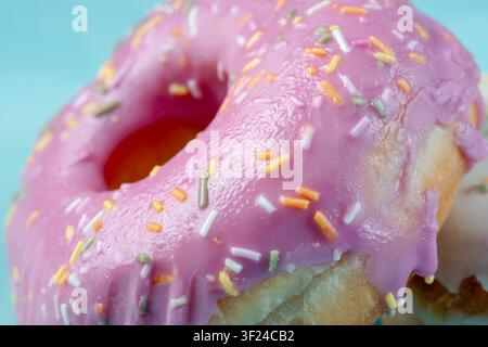 Extreme close up detailing the shiny texture of pink fruit icing and multi-colored sweet sprinkles on a fresh pastry Stock Photo