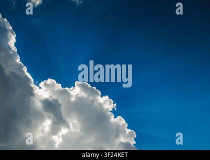 Dramatic blue sky with sun rays shining through fluffy white clouds Stock Photo