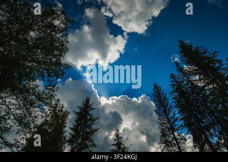 Dramatic blue sky with sun rays shining through fluffy white clouds Stock Photo