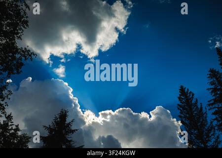 Dramatic blue sky with sun rays shining through fluffy white clouds Stock Photo