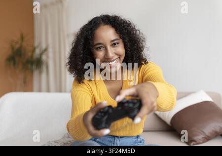 Smiling Young Black Woman Playing Video Game At Home With Game Controller, Relaxation Concept Stock Photo