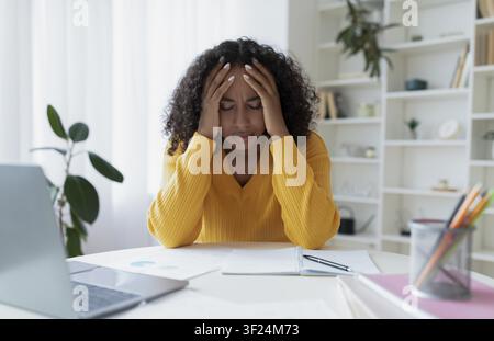 Worried Black Woman With Curly Hair Holding Head While Working At Home Office, Stress Concept Stock Photo