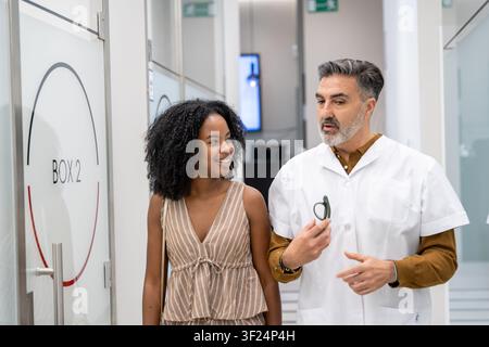 Doctor and young woman walking in clinic hallway, discussing medical advice Stock Photo