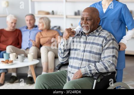 Happy African American Senior Man In Wheelchair Smiling With Caregiver, Healthcare Concept Stock Photo