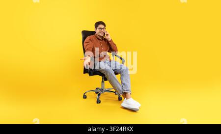 Young Man Sitting On Chair Talking On Phone In Office, Business Concept Stock Photo