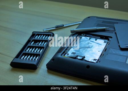 Preparing for a laptop hardware upgrade. A precision screwdriver kit and a disassembled laptop showing an exposed internal hard drive bay lay ready on Stock Photo