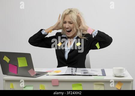 Stressed Caucasian Woman In Suit At Desk Trying To Work With Laptop, Office Background Stock Photo